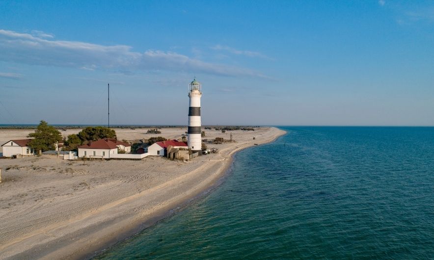 Біля морського узбережжя стоїть маяк і кілька будинків