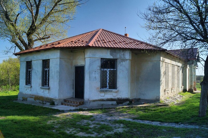 Звичайний сільський пошарпаний будинок, білі стіни, червоний дах. Навколо дерева