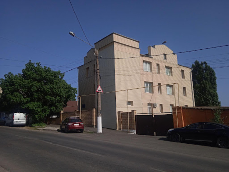 Триповерховий білий будинок поруч із асфальтованою дорогою. На узбіччі машини