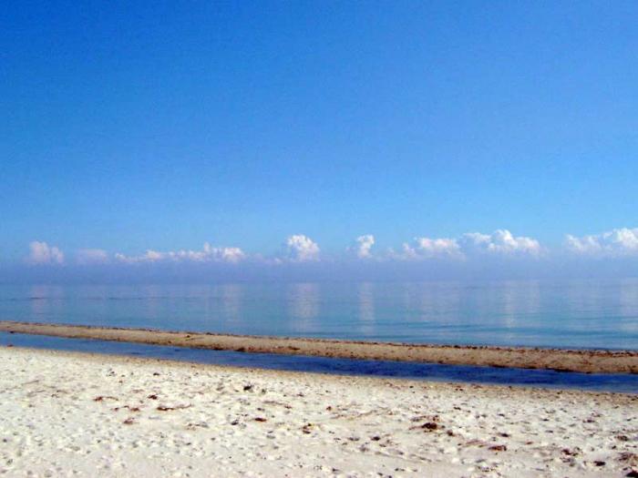 Білий пісок узбережжя, поруч прозора вода й блакитне небо