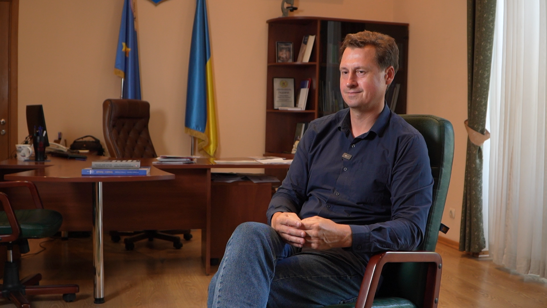 Чоловік сидить у кріслі в кабінеті й злегка посміхається