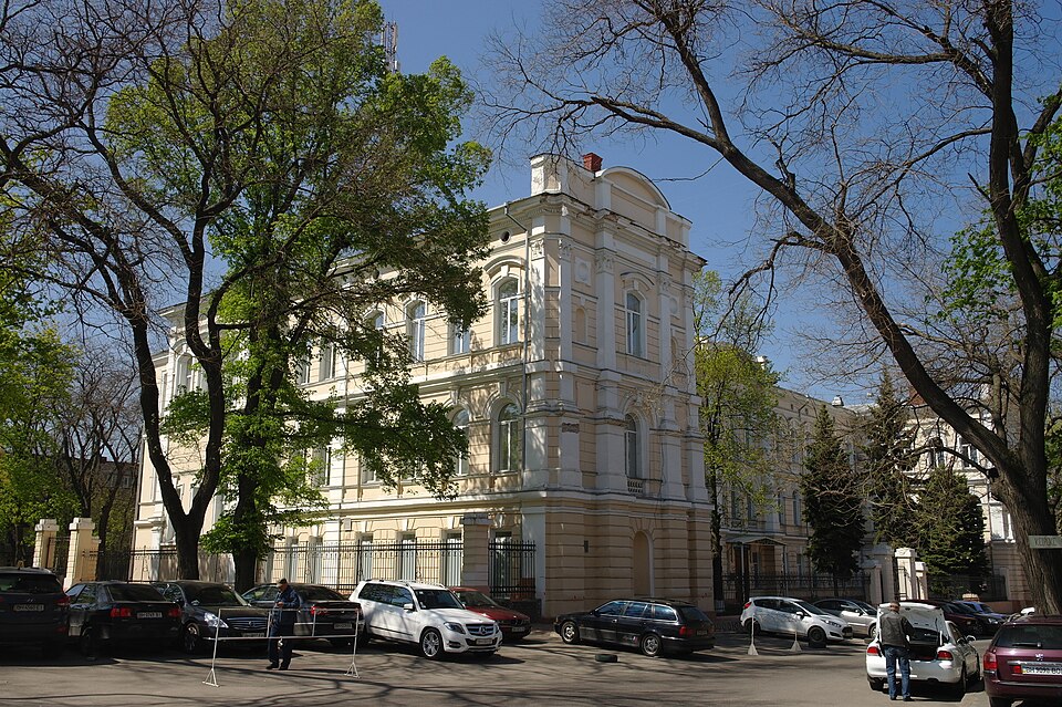 Триповерховий білий будинок, поруч автівки
