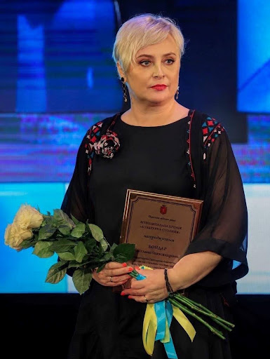 Жінка стоїть із грамотою і квітами