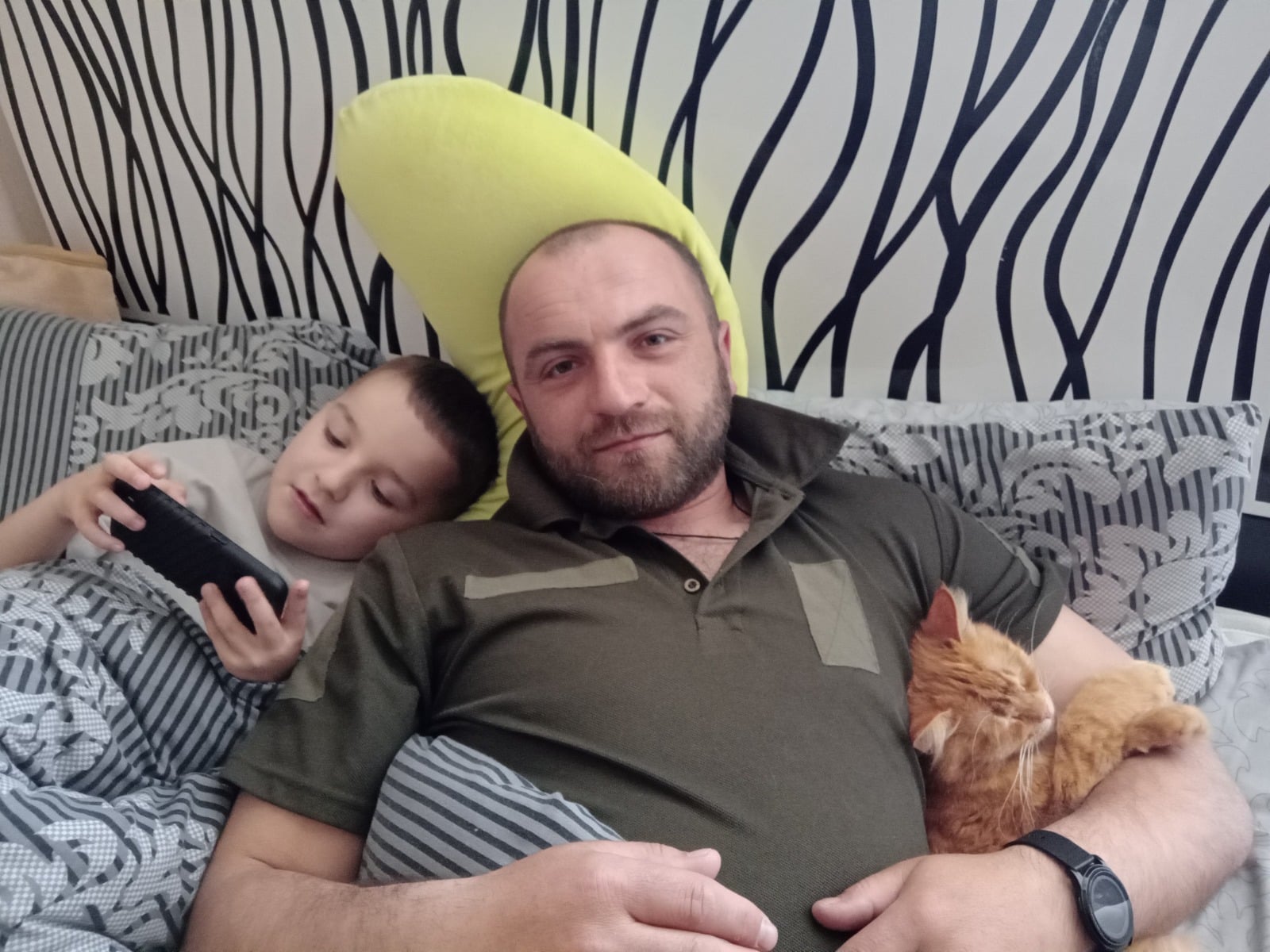 На ліжку чоловік, його син і кіт
